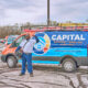 A worker gives a thumbs up and holds a tool bag while standing in front of a Capital Heating, Cooling, and Electric van in a Milwaukee parking lot.