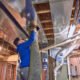 A professional diligently cleans the ducts in a basement, using a large hose connected to the ductwork.