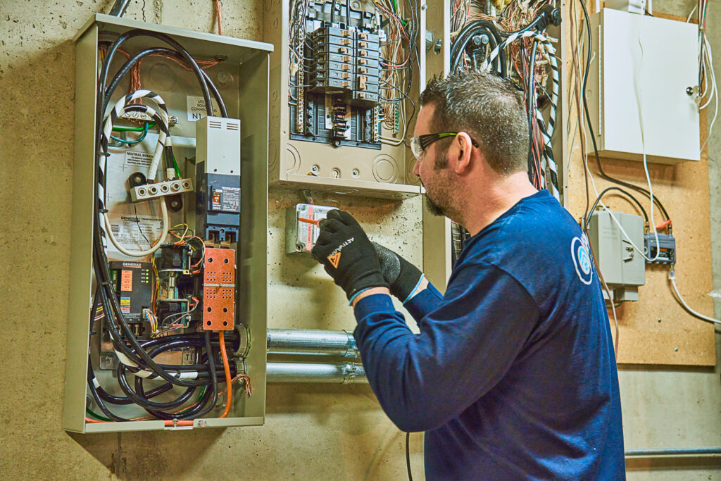 The electrician intensely examines a circuit breaker panel, wearing protective gloves and glasses in the utility room. With expertise in smart homes, the electrician optimizes surge protection to meet modern safety standards.