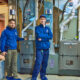 Two technicians in blue uniforms stand in front of heating and cooling systems, including a furnace, in a basement. They are ready to maintain the equipment and ensure everything runs smoothly for the upcoming winter season.